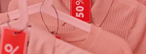 Zbliżenie na różowe ubrania z czerwonymi napisami „50%” na białych wieszakach. Zbliżenie na różowe ubrania z czerwonymi napisami „50%” na białych wieszakach.