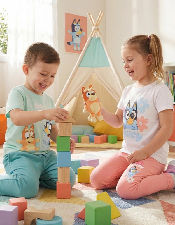 Dwoje dzieci bawi się razem na kolorowym dywaniku, układając klocki i trzymając zabawkę w jasnym i radosnym pokoju.