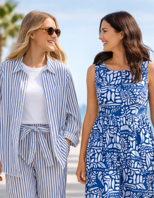 Dwie kobiety spacerują w letnich stylizacjach wzdłuż nadmorskiej promenady – lekka moda na stylowe i beztroskie chwile wakacyjne
