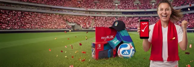 Osoba na stadionie trzyma smartfon z aplikacją myKiK, otoczona konsolą Nintendo Switch, piłką nożną, czapką, szalikiem i paczką myKiK.