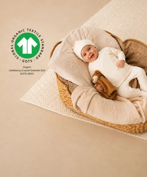 Niemowlę w odzieży z bawełny organicznej z certyfikatem GOTS leży w plecionym koszu z przytulanką